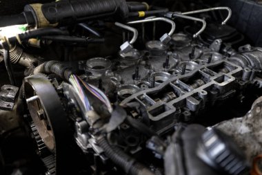 Parçalanmış bir dizel kamyon motoru işlek bir tamirhanede ya da depoda ahşap desteklerin üzerinde yatıyor ve arka planda eğimli bir kamyon taksisi görünüyor.