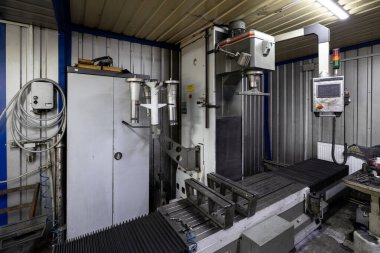 Parçalanmış bir dizel kamyon motoru işlek bir tamirhanede ya da depoda ahşap desteklerin üzerinde yatıyor ve arka planda eğimli bir kamyon taksisi görünüyor.