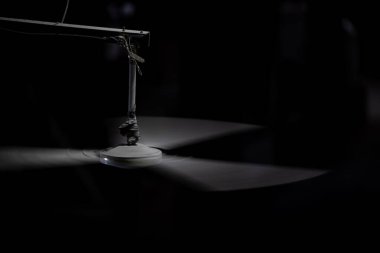 Üç pervaneli bir endüstriyel tavan pervanesi tek bir ışıkla aydınlatılan karanlık bir arka plana doğru hızla dönüyor..