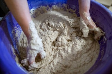 El yapımı ekmek hazırlama işlemi sırasında büyük plastik bir kabın içinde hamur yoğuran eller. Hamur yapış yapış ve yapış, aktif karışımı gösteriyor..
