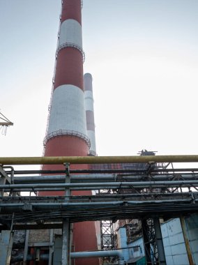 Yüksek kapasiteli bir termik santralde devasa bir gaz egzoz sistemi. Yüksek kırmızı-beyaz bacalar 150 metreyi aşarak emisyon yönetimi ve endüstriyel hava dolaşımını kolaylaştırıyor..
