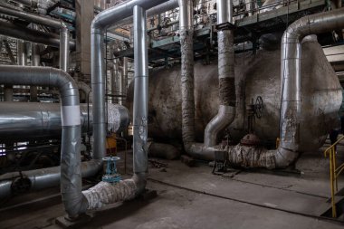 Endüstriyel ortamda birbirine bağlı büyük metal borular ve makineler. Yalıtımlı supap ve tesisatlı boru hatları, fabrika veya işleme tesisi içinde sıvı veya gaz taşımacılığı öneriyor.