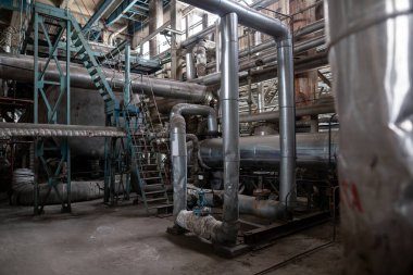 Endüstriyel ortamda birbirine bağlı büyük metal borular ve makineler. Yalıtımlı supap ve tesisatlı boru hatları, fabrika veya işleme tesisi içinde sıvı veya gaz taşımacılığı öneriyor.