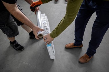 Metal-plastik veya PVC pencereler için üretim alanı, genellikle vinil pencere olarak bilinir. Plastik bir pencereyi paketleyen iki işçi, çerçevenin etrafındaki koruyucu ambalajı sağlama alıyor..