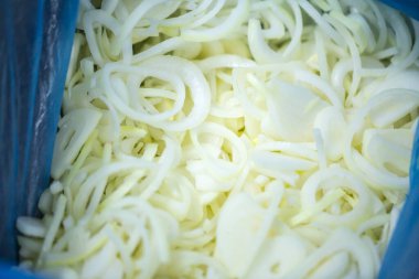 Donmuş soğan halkaları ve ince buz kaplamalı yarım halkalar yakın çekim. Süpermarketlerde raf ömrünün uzatılması ve bozulabilir hasat kalitesinin korunması için perakende paketlemeye hazırlar..