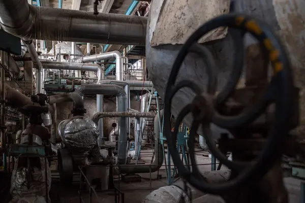 Endüstriyel ortamda birbirine bağlı büyük metal borular ve makineler. Yalıtımlı supap ve tesisatlı boru hatları, fabrika veya işleme tesisi içinde sıvı veya gaz taşımacılığı öneriyor.