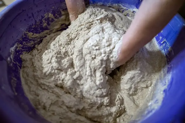 El yapımı ekmek hazırlama işlemi sırasında büyük plastik bir kabın içinde hamur yoğuran eller. Hamur yapış yapış ve yapış, aktif karışımı gösteriyor..