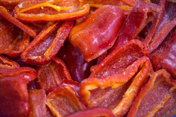 Dondurulmuş kırmızı biber parçalarının yakın planında ince bir buz tabakası ve korunmuş tazelik. Perakende satışlar ve bozulabilir hasatların korunması için uzun raf ömrü sağlamak üzere ambalaj işlemine hazırlandı.