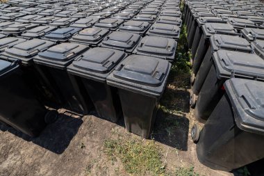 Atık temizleme servisi için bir depolama tesisinde sıraya dizilmiş çok sayıda siyah çöp bidonu. Düzenli bir şekilde dağıtım ya da toplama için hazırlar..