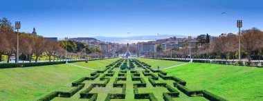 Eduardo VII Park gözlem güvertesinden Lizbon, Portekiz 'in panoramik şehir manzarası. Çeşitli binalar, merkezi simgeler ve uzak Tagus Nehri 'nin yer aldığı simetrik çitler..