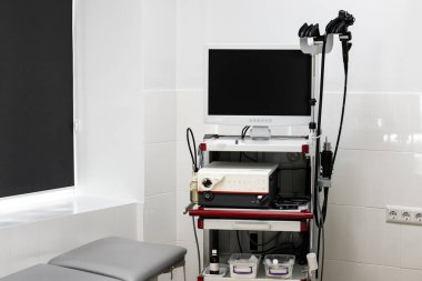 Geniş bir monitörü, işleme ünitesi ve endoskopisi olan modern bir endoskopi sistemi, duvarları fayanslarla kaplı, temiz bir tıbbi odadaki seyyar bir arabada bulunuyor..
