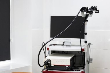 Geniş bir monitörü, işleme ünitesi ve endoskopisi olan modern bir endoskopi sistemi, duvarları fayanslarla kaplı, temiz bir tıbbi odadaki seyyar bir arabada bulunuyor..