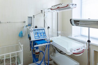 Temiz, boş bir hastane kuluçka odasında bebek beşiği, bebek ısıtıcısı ve solunum cihazının yanında bulunur..