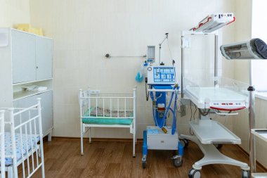 Temiz, boş bir hastane kuluçka odasında bebek beşiği, bebek ısıtıcısı ve solunum cihazının yanında bulunur..