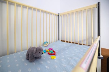 Bebek ya da küçük çocuklar için tasarlanmış boş bir hastane yatağında steril bir odaya yerleştirilmiş hafif raylar, desenli bir yatak ve oyuncaklar yer alıyor..