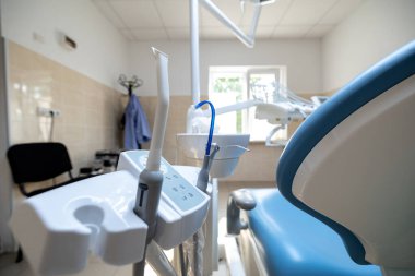 Modern bir diş sağlığı kliniğinde, parlak ve temiz bir tedavi odasında vakum ve el aletleri de dahil olmak üzere ilişkili araçlarla birlikte mavi bir diş sağlığı koltuğu bulunur..