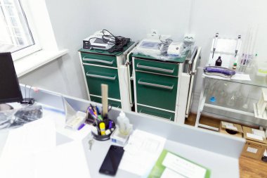 Yeşil çekmeceli iki tıbbi araç temiz bir klinik odasında laboratuvar ekipmanı, tüp rafları ve çeşitli tıbbi malzemeler bulundurur.