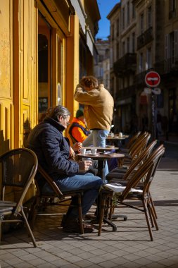 Bordeaux, Fransa - 23 Kasım 2021: İnsanlar tarihi binaları olan güneşli bir cadde olan Fernand Rey Meydanı 'ndaki Bar L' Apollo Kafe 'nin açık masalarında oturuyorlar..