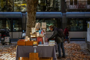 Bordeaux, Fransa - 23 Kasım 2021: Jean Moulin Meydanı 'ndaki açık hava kitap pazarı, insanların kitap baktığı bir sonbahar ağacı ve arka planda bir heykel. Bordeaux, Gironde, Yeni Aquitaine, Fransa.