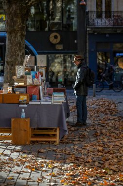 Bordeaux, Fransa - 23 Kasım 2021: Jean Moulin Meydanı 'ndaki açık hava kitap pazarı, insanların kitap baktığı bir sonbahar ağacı ve arka planda bir heykel. Bordeaux, Gironde, Yeni Aquitaine, Fransa.