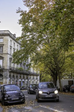 Bordeaux, Fransa - 23 Kasım 2021: Place des Quinconces caddesi, sonbahar ağaçları ve park edilmiş arabalarla dolu, kemerli klasik mimari. Bordeaux, Gironde, Yeni Aquitaine, Fransa.