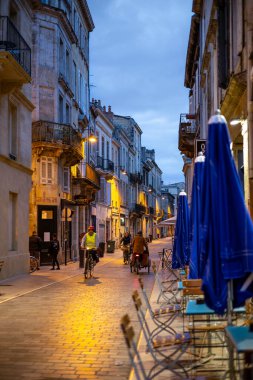 Bordeaux, Fransa - 23 Kasım 2021: Rue du Ha 'da akşam sokak manzarası, klasik binalar ve ışıklandırılmış sokak lambaları, bisikletçiler, yayalar ve mavi şemsiyeli bir açık hava kafe. Bordeaux, Gironde, Yeni Aq