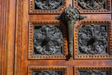 Karmaşık ahşap bir kapı süslü oymalar, dekoratif metal kollar ve büyük bir boynuz şeklinde bronz sapı vardır..