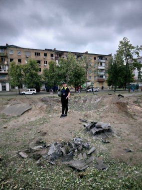 Kyiv, Ukrayna - 17 Haziran 2025: Bir polis memuru, arka planda hasarlı bir yerleşim binası bulunan Rus krateri ve füze patlamasının enkazı yakınında duruyor.
