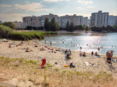 Kyiv, Ukrayna - 14 Temmuz 2025: Sonyachne Gölü 'nde sıcak temmuz öğleden sonra dinlenen ve yüzen insanların olduğu kumlu bir sahil. Arka planda yüksek binalar var..