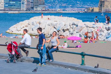 Napoli, İtalya - 27 Mayıs Akdeniz kıyısında yaz günü. İnsanlar rahatlar, yürürler, güneşlenirler ve deniz kenarındaki hayatın tadını çıkarırlar. Bebek arabasında çocuklu ebeveynler. 27 Mayıs 2012. Napoli, Campania, İtalya.