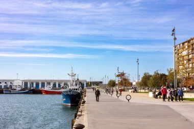 Santander, İspanya - 20 Kasım 2021: İnsanlar güneşli bir sonbahar gününde balıkçı limanının geniş rıhtımında gezinirler. Balıkçı tekneleri rıhtıma demirlemiş. Liman şehrinde günlük bir hayat.