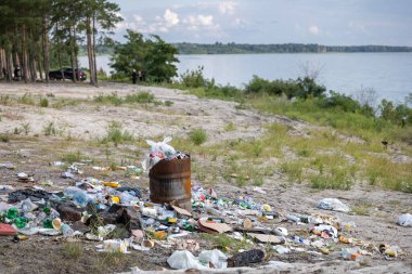 Çamur bir göl kıyısını boğuyor. Etrafa saçılmış plastik ve atıklar arasında fazla doldurulmuş varil. Doğanın güzelliğini ve ekosistem sağlığını göz ardı eden insanların acı dolu bir çevre ihmali sahnesi..