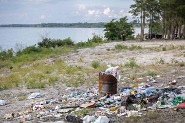 Üzücü bir kirlilik sahnesi. Plastik şişeler ve atıklarla dolu bir halının arasında paslı bir fıçı taşar. Bu da insanların doğal ekosistemi umursamadıklarını hatırlatır..