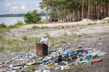 Üzücü bir kirlilik sahnesi. Plastik şişeler ve atıklarla dolu bir halının arasında paslı bir fıçı taşar. Bu da insanların doğal ekosistemi umursamadıklarını hatırlatır..