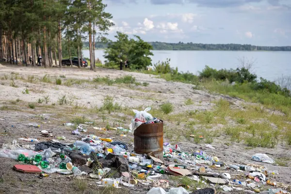 Çamur bir göl kıyısını boğuyor. Etrafa saçılmış plastik ve atıklar arasında fazla doldurulmuş varil. Doğanın güzelliğini ve ekosistem sağlığını göz ardı eden insanların acı dolu bir çevre ihmali sahnesi..