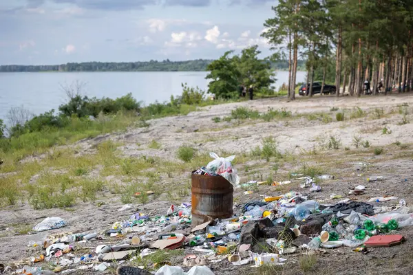 Üzücü bir kirlilik sahnesi. Plastik şişeler ve atıklarla dolu bir halının arasında paslı bir fıçı taşar. Bu da insanların doğal ekosistemi umursamadıklarını hatırlatır..