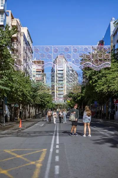 Alicante, İspanya 14 Kasım 2021: Melia tarafından Alicante 'de bulunan Alicante Gran Sol Oteli' nin cephesinde büyük bir duvar resmi bulunmaktadır. Noel ışıkları olan cadde restoran ve dükkanlarla dolu..