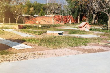 Terk edilmiş mini golf sahasında aşırı büyümüş çimenler, beton yollar ve ev şeklinde bir yapı gibi küçük engeller var. Sahne ağaçlar ve tuğla bir duvarla çevrili..