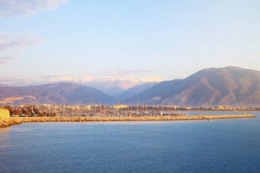 Finike marinası sabahın erken saatlerinde, açık bir gökyüzünün altında kar kaplı dağlarla altın güneş ışığıyla yıkanırken görülüyor..