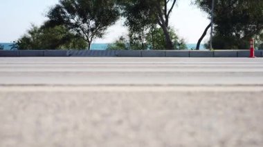 Çok düşük bir açıdan çekilen 4K video görüntüsü, araçların alt kısımlarını yoldan geçerken gösteriyor. Video bulanık, ağaçlar ve Akdeniz ile yer seviyesine odaklı.