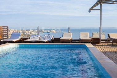 Şehir manzarasına bakan çatı havuzu ve şezlonglarla okyanus ufku.