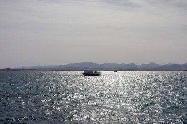 Parlak su ufkunda teknelerle sakin bir okyanus manzarası.