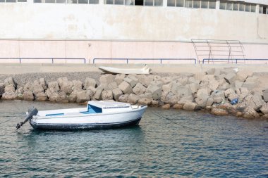 Kayalık kıyı şeridine demirlemiş beyaz kayıkla sakin bir sahil manzarası