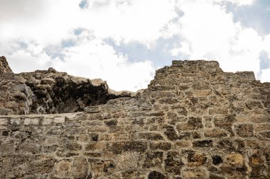 Bulutlu mavi gökyüzüne karşı antik taş kale duvarları.