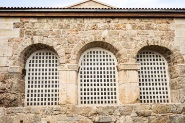 Üç kemerli pencere ve ızgaralı tarihi taş bina.