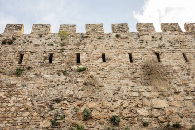 Mavi gökyüzünün altında siperleri ve ok yarıkları olan antik taş kale duvarı..