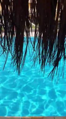 Dalgalı havuz suyu saman çatısı ardında görünüyor..