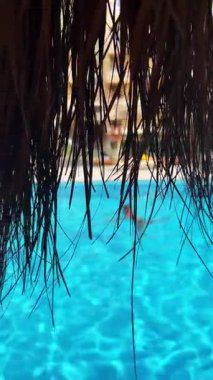 Yüzücülerin sazdan çatıya çıktığı mavi havuz manzarası.