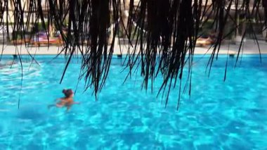 Yüzücüler güneşli bir günde havuzun tadını çıkarırlar. Sazlı çatıya odaklan. Arkaplan videosu.