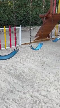 Kumlu yüzeyde salıncaklı ve tırmanan bir oyun alanı.